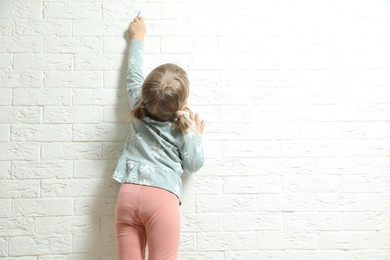 Photo of Little girl drawing on white brick wall, back view and space for text. Child`s art