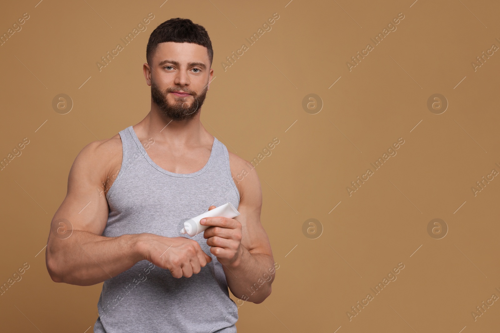 Photo of Handsome man applying body cream onto his hand on pale brown background, space for text