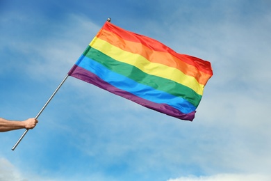 Photo of Gay man holding rainbow LGBT flag against blue sky