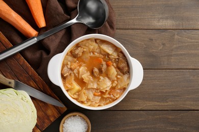 Photo of Tasty cabbage soup and ingredients on wooden table, flat lay. Space for text