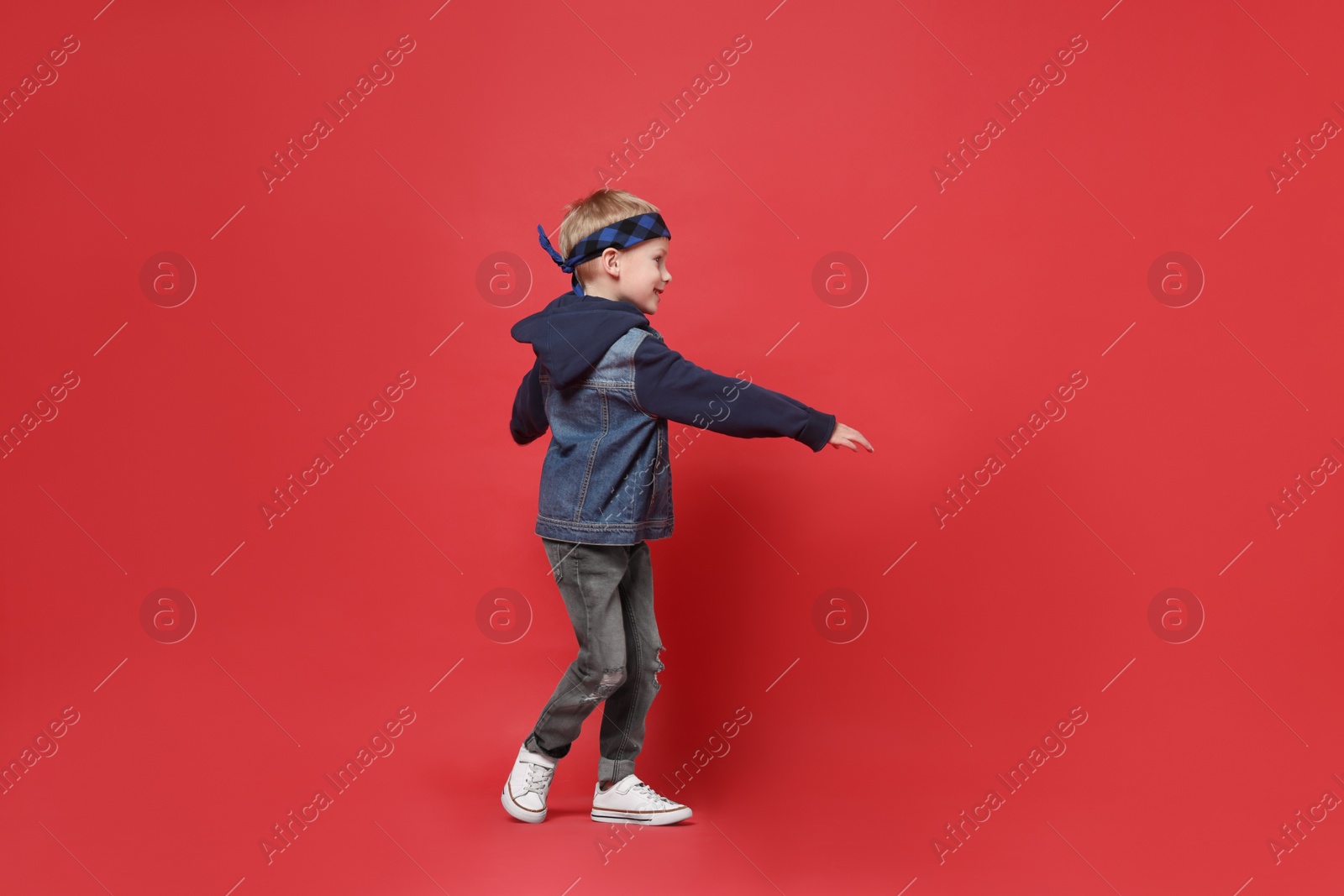 Photo of Happy little boy dancing on red background. Space for text