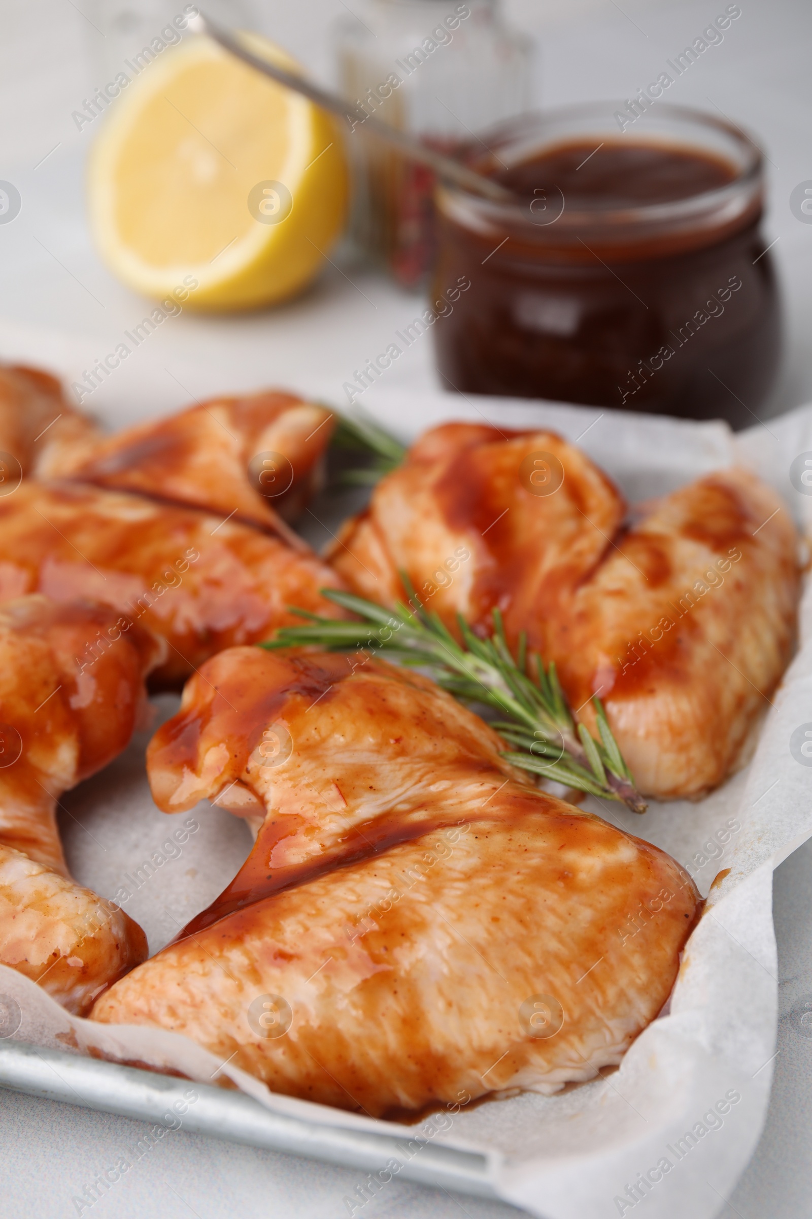 Photo of Raw marinated chicken wings and rosemary on light table, closeup