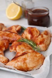 Photo of Raw marinated chicken wings and rosemary on light table, closeup