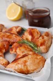 Raw marinated chicken wings and rosemary on light table, closeup