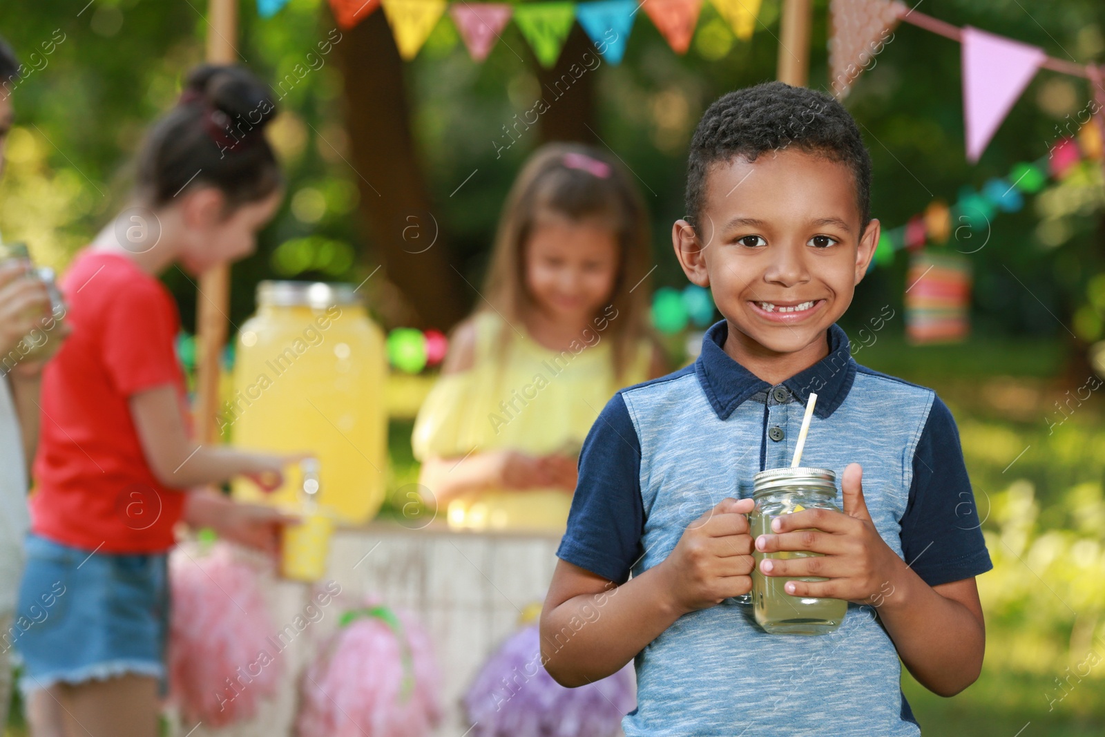 Photo of Cute little African-American boy with natural lemonade in park, space for text. Summer refreshing drink