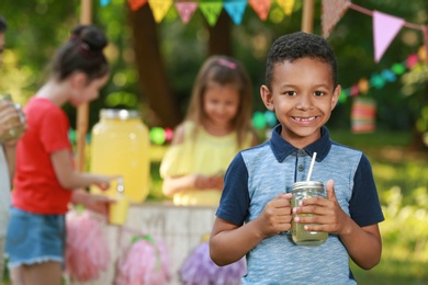 Cute little African-American boy with natural lemonade in park, space for text. Summer refreshing drink