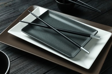 Photo of Stylish sushi dishware and chopsticks on black wooden table, closeup