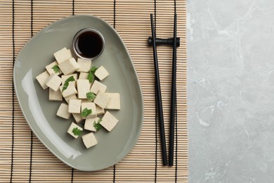Delicious tofu with parsley, soy sauce and chopsticks on grey marble table, flat lay