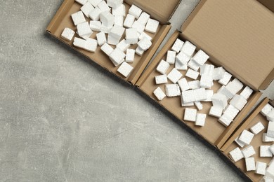 Photo of Many open cardboard boxes with pieces of polystyrene foam on grey textured background, flat lay. Space for text