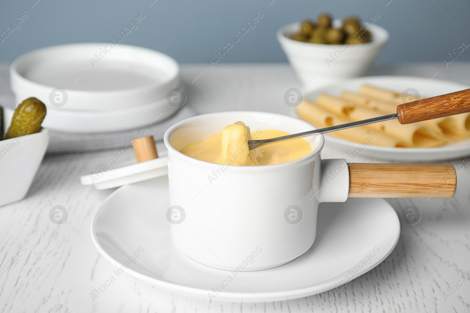 Photo of Pot of tasty cheese fondue and fork with bread on white wooden table