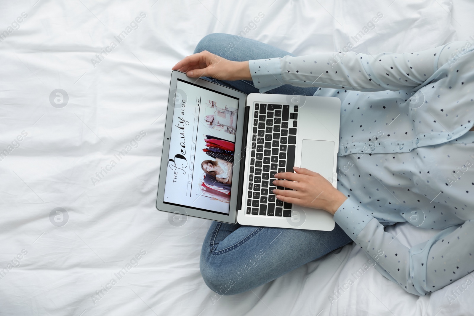 Photo of Woman holding laptop with open beauty blogger site on bed, top view. Space for text