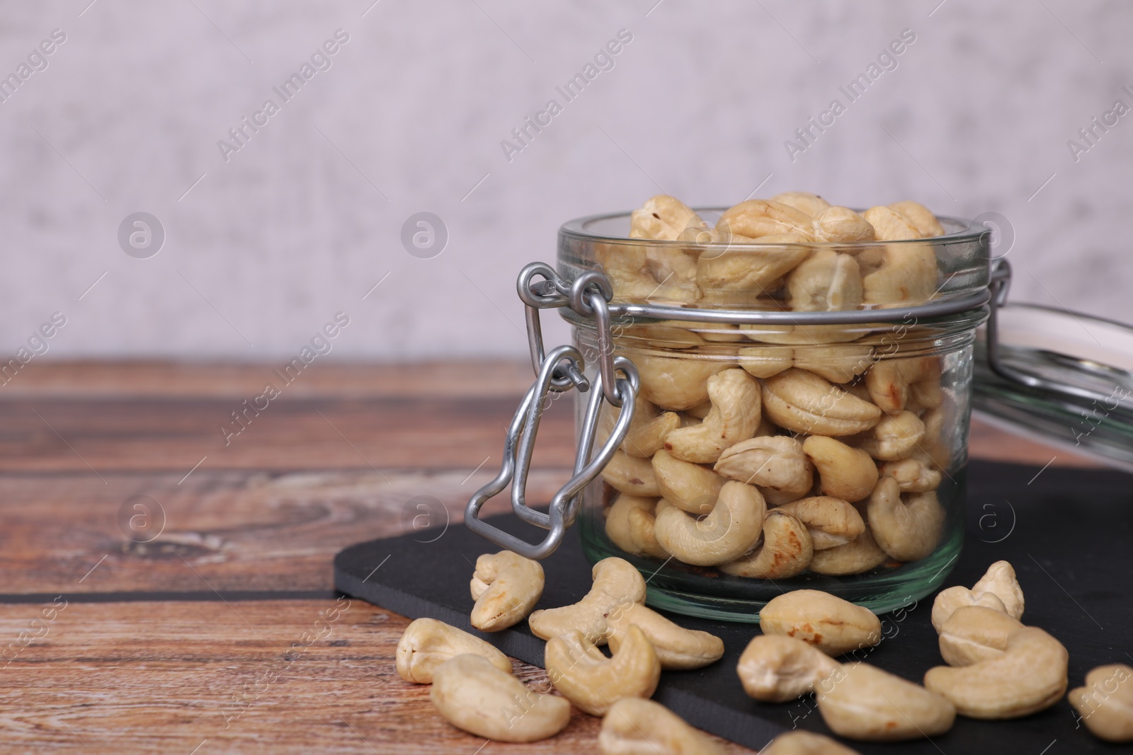 Photo of Tasty cashew nuts in glass jar on wooden table, space for text