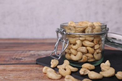 Photo of Tasty cashew nuts in glass jar on wooden table, space for text