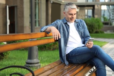 Photo of Portrait of handsome mature man using mobile phone in city. Space for text