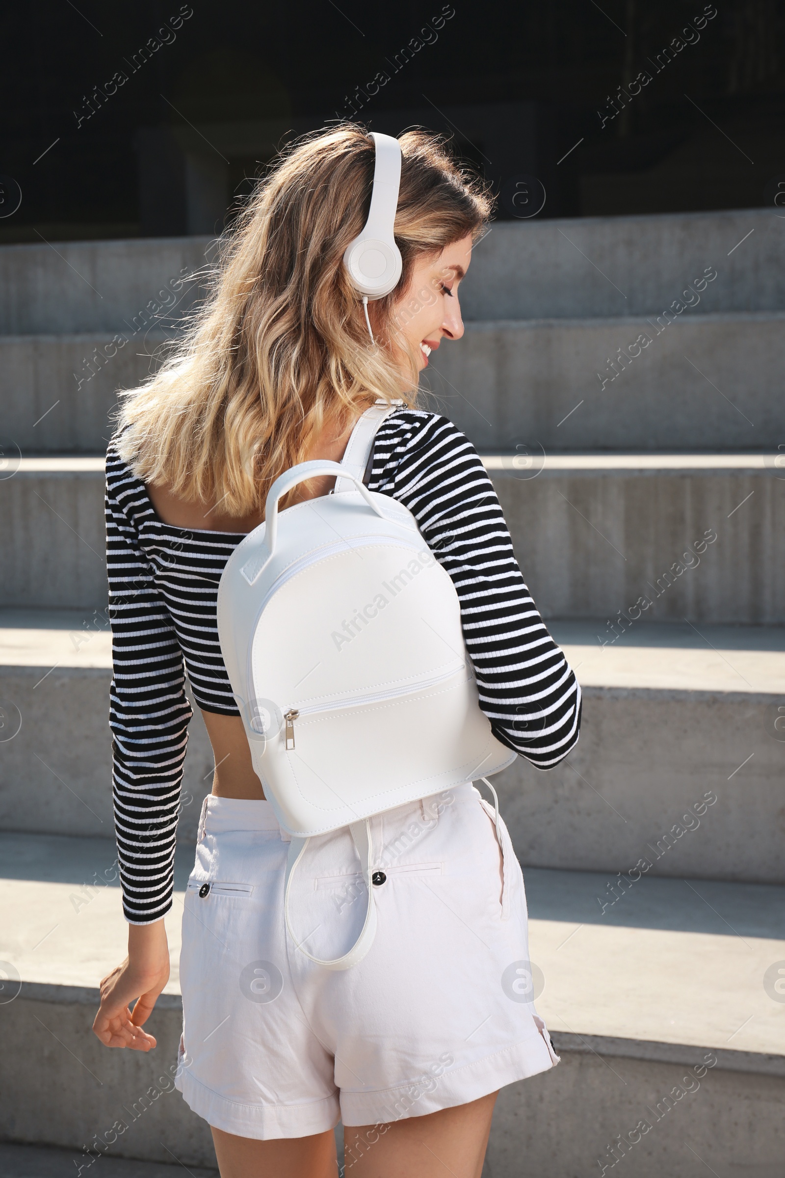 Photo of Young woman with stylish backpack on stairs outdoors, back view