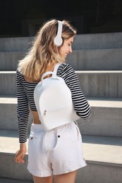 Young woman with stylish backpack on stairs outdoors, back view