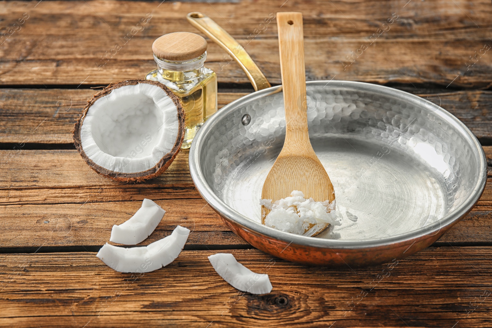 Photo of Frying pan with coconut oil and nut pieces on wooden background