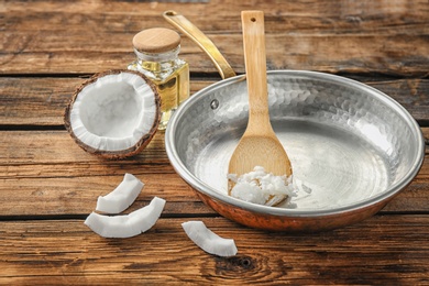 Frying pan with coconut oil and nut pieces on wooden background