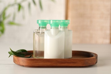 Mini bottles of cosmetic products on white table against blurred background