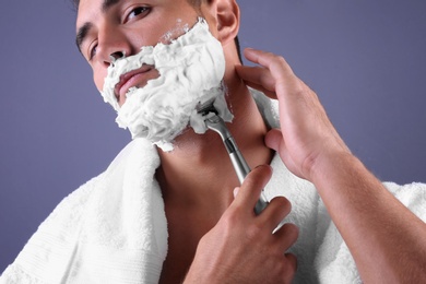 Handsome young man shaving on color background, closeup