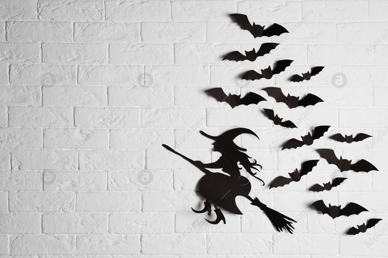 Photo of Paper bats and witch cutout on brick wall with space for text. Halloween decor