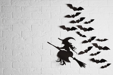 Paper bats and witch cutout on brick wall with space for text. Halloween decor