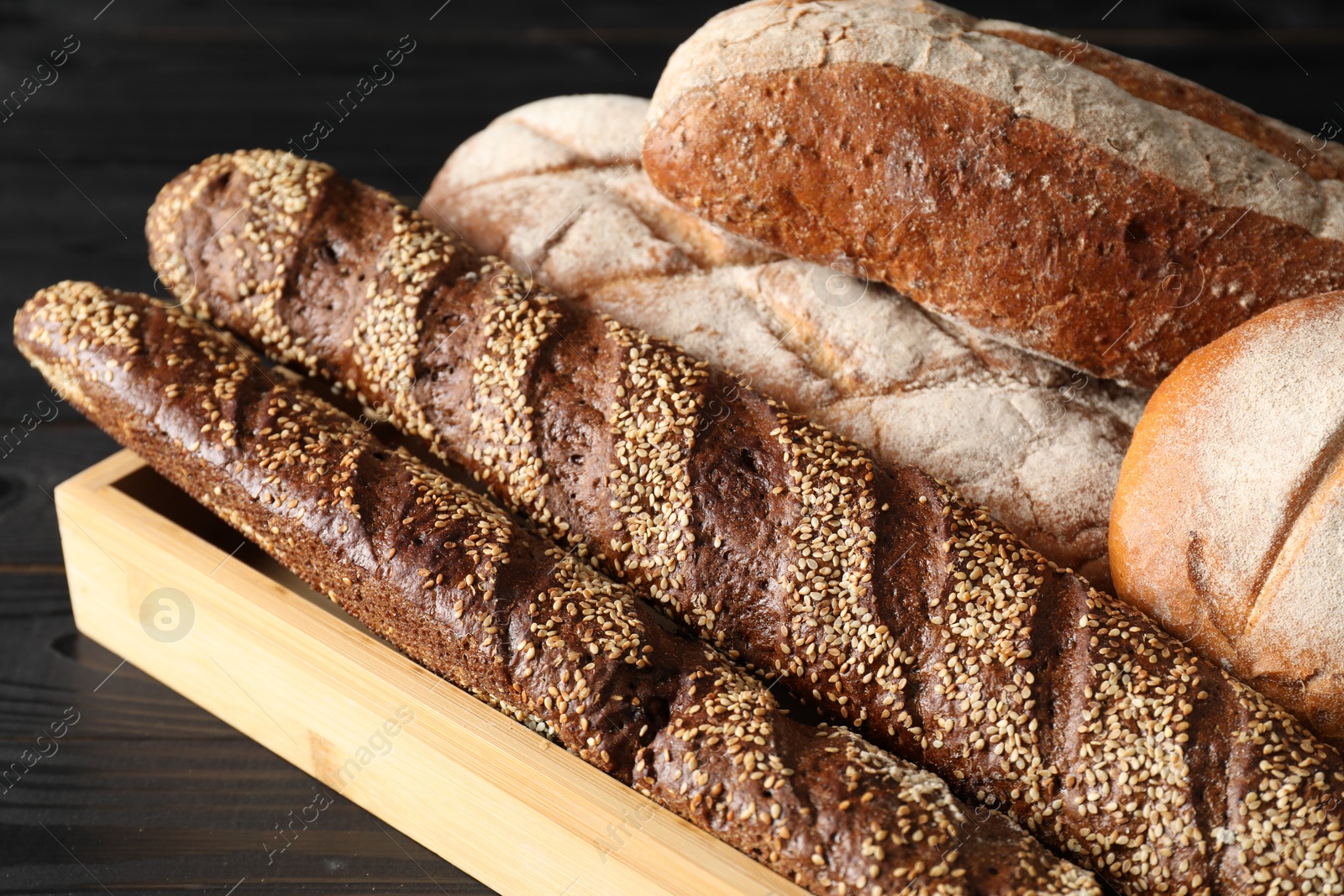 Photo of Basket with different types of fresh bread on black wooden table