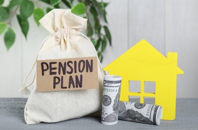 Photo of Card with phrase Pension Plan, sack, dollar banknotes and yellow house figure on light blue wooden table. Retirement concept