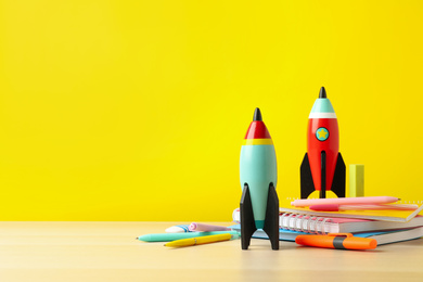 Photo of Bright toy rockets and school supplies on wooden table. Space for text