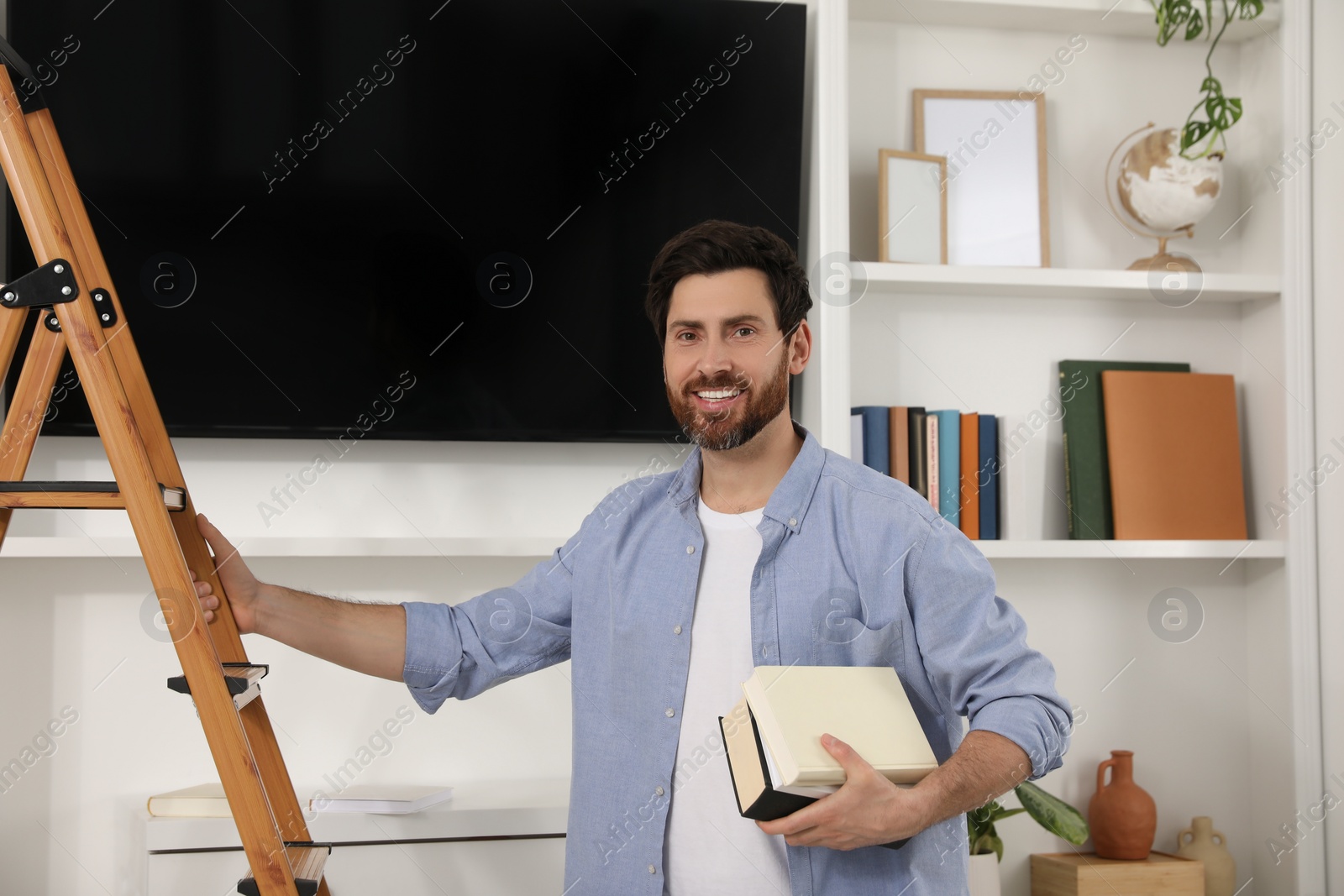 Photo of Happy man with books near wooden folding ladder indoors