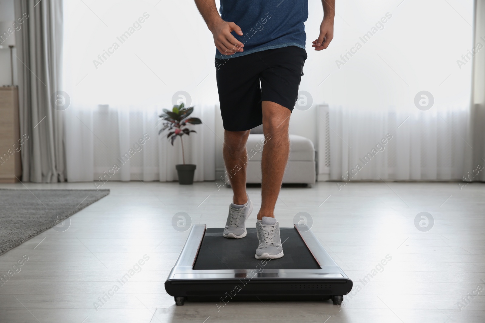 Photo of Sporty man training on walking treadmill at home, closeup