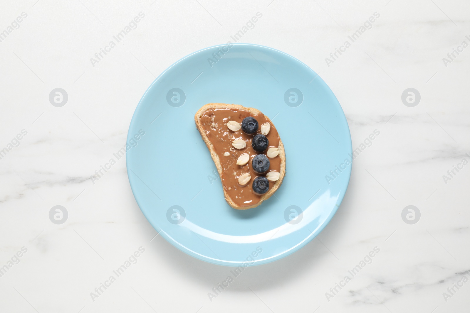 Photo of Toast with tasty nut butter, blueberries and peanuts on white marble table, top view