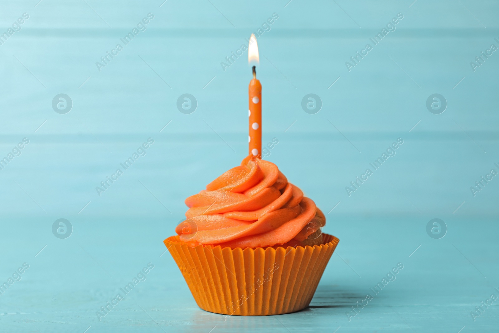 Photo of Delicious birthday cupcake with cream and burning candle on blue wooden background