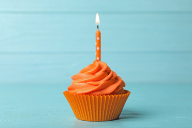 Photo of Delicious birthday cupcake with cream and burning candle on blue wooden background