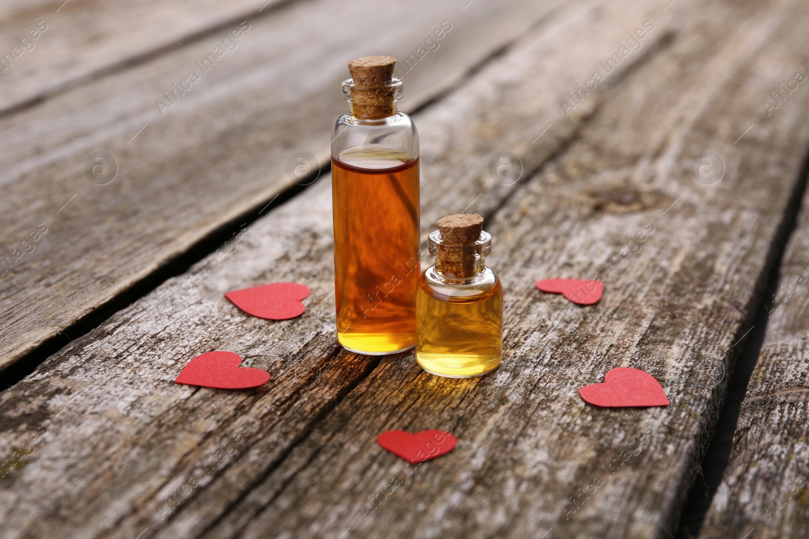 Photo of Bottles of love potion and paper hearts on wooden table