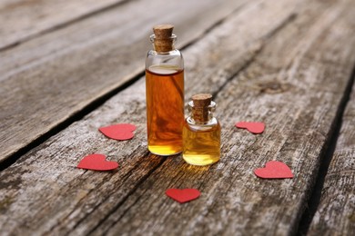 Photo of Bottles of love potion and paper hearts on wooden table