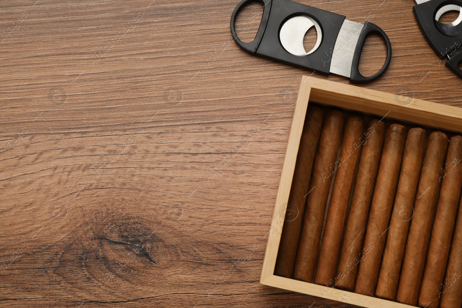 Photo of Box with cigars and guillotine cutters on wooden table, flat lay. Space for text