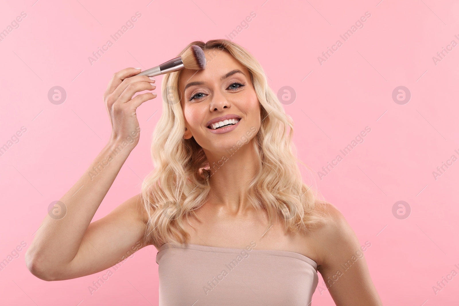 Photo of Beautiful makeup. Smiling woman with brush on pink background