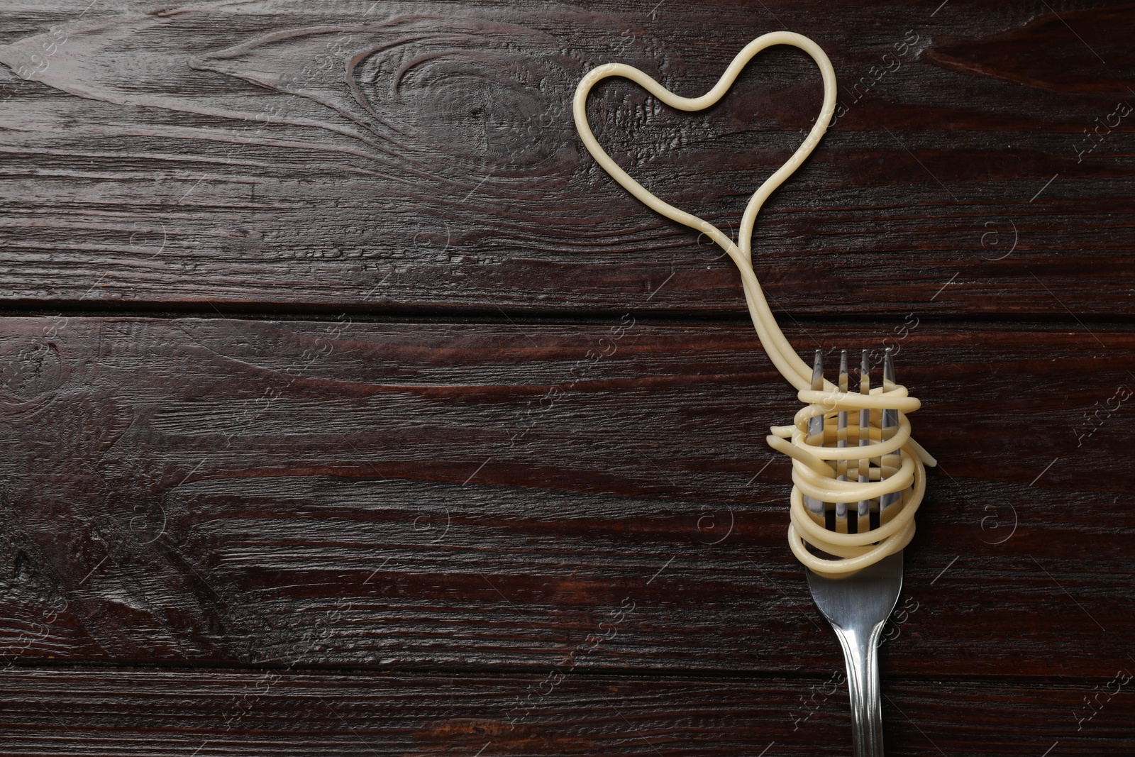 Photo of Heart made of tasty spaghetti and fork on wooden table, top view. Space for text