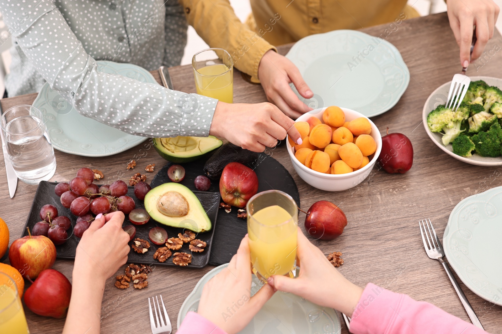 Photo of Friends eating vegetarian food at wooden table indoors, closeup