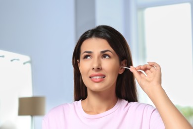 Photo of Young woman cleaning ear with cotton swab indoors