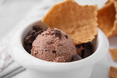 Tasty chocolate ice cream and piece of waffle cone in bowl, closeup