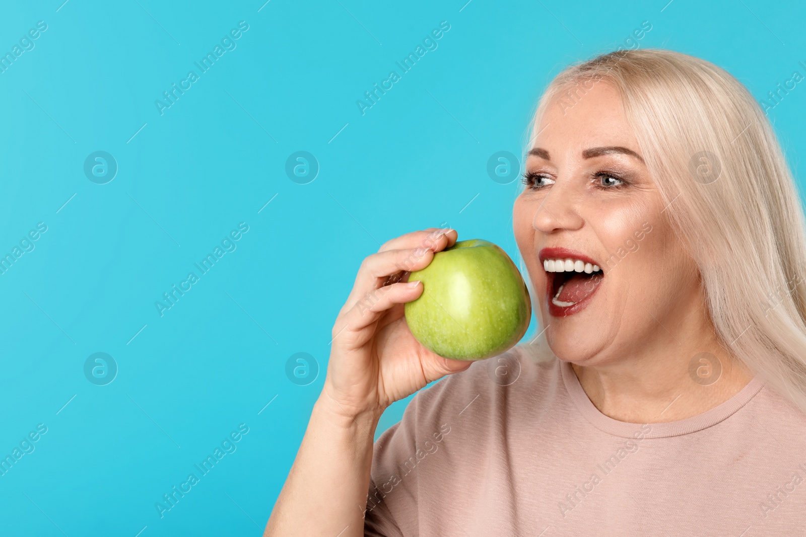 Photo of Smiling woman with perfect teeth and green apple on color background. Space for text