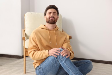 Photo of Man suffering from leg pain on carpet indoors