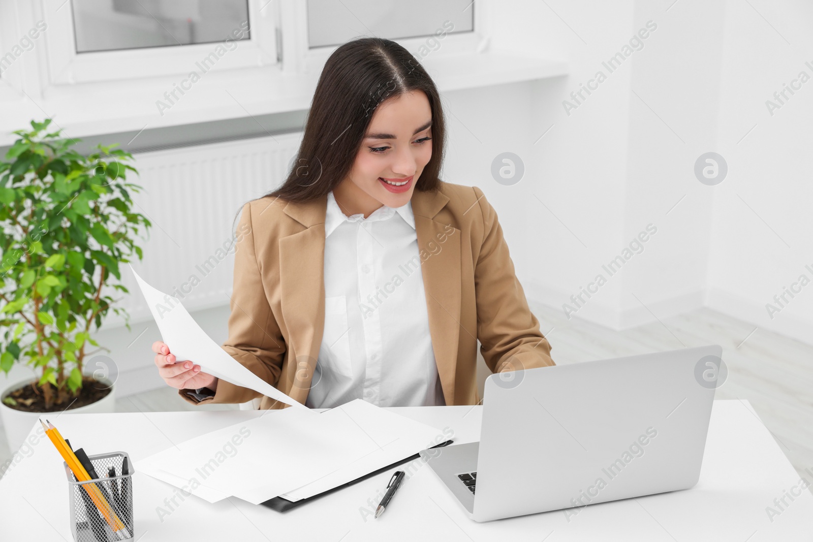 Photo of Young female intern working with laptop at table in office