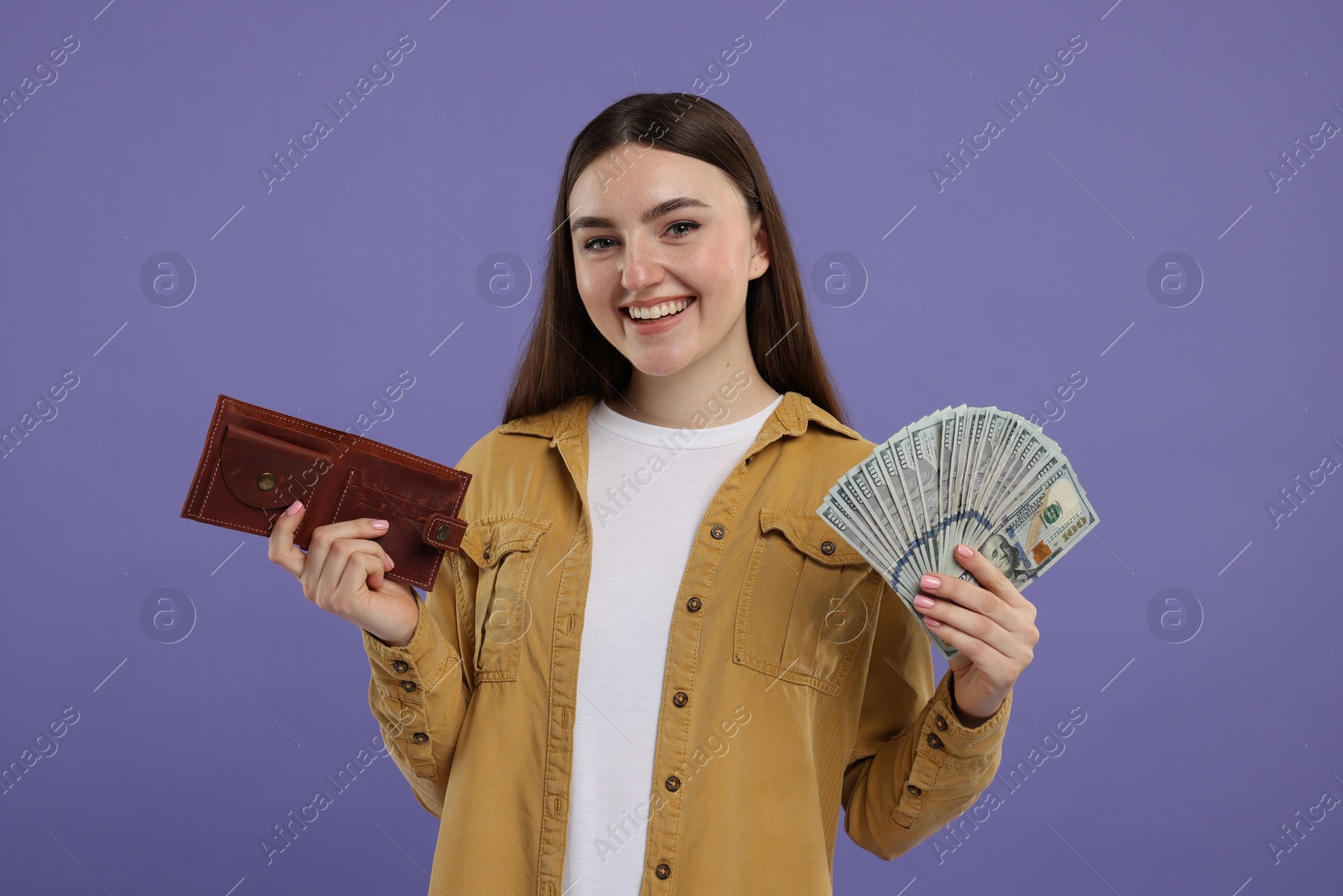 Photo of Happy woman with wallet and dollar banknotes on purple background