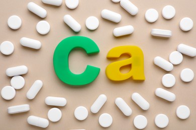 Photo of Pills and calcium symbol made of colorful letters on beige background, flat lay