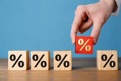 Image of Best mortgage interest rate. Woman putting red cube with percent sign among others on wooden table, closeup