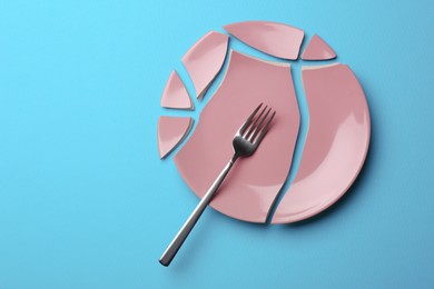Photo of Pieces of broken ceramic plate and fork on light blue background, flat lay. Space for text