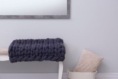 Photo of Knitted merino wool plaid on bench near grey wall